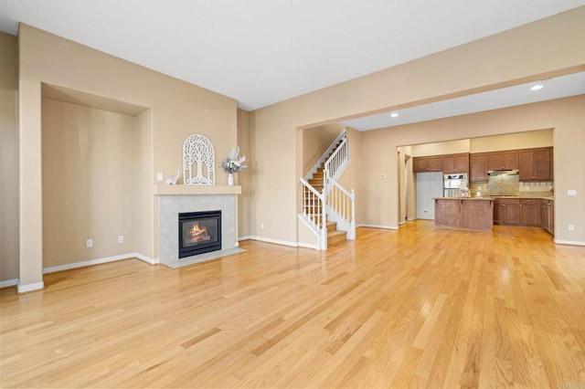 unfurnished living room with light wood-style floors, baseboards, stairway, and a tile fireplace