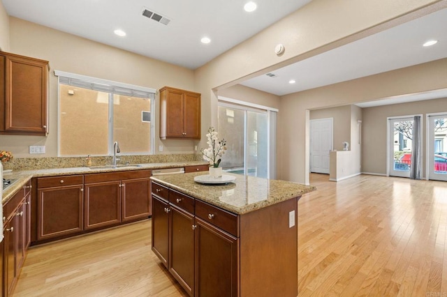 kitchen with light wood-type flooring, visible vents, a sink, and a center island