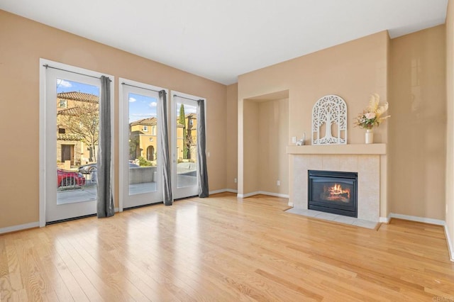 unfurnished living room with a tile fireplace, baseboards, and wood finished floors