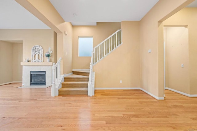 interior space with light wood-style floors, a tile fireplace, stairway, and baseboards