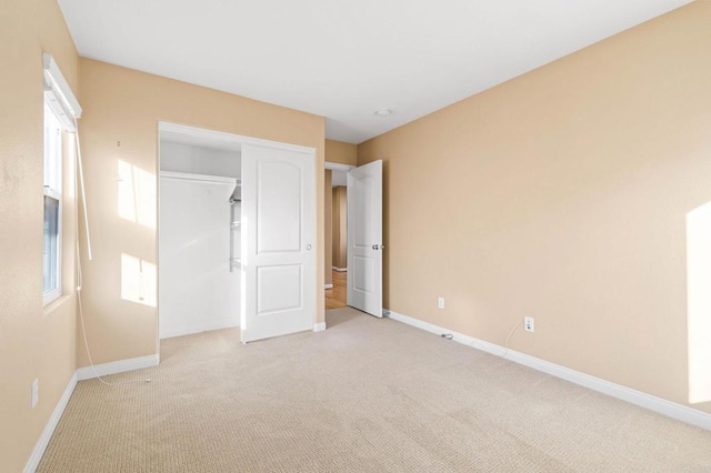 unfurnished bedroom featuring baseboards, multiple windows, a closet, and light colored carpet