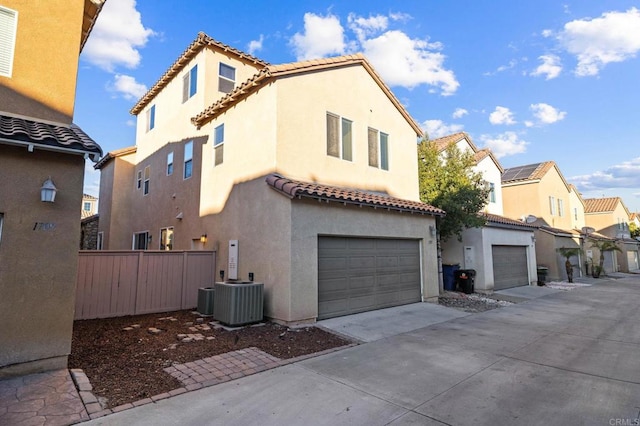 view of front of home featuring stucco siding, concrete driveway, an attached garage, central AC, and a residential view