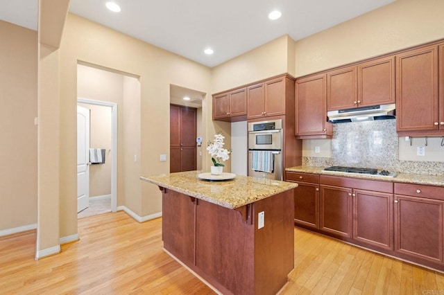 kitchen featuring a kitchen island, appliances with stainless steel finishes, a kitchen breakfast bar, light stone countertops, and under cabinet range hood