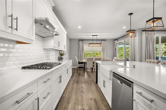 kitchen featuring appliances with stainless steel finishes, dark wood-type flooring, hanging light fixtures, white cabinets, and sink