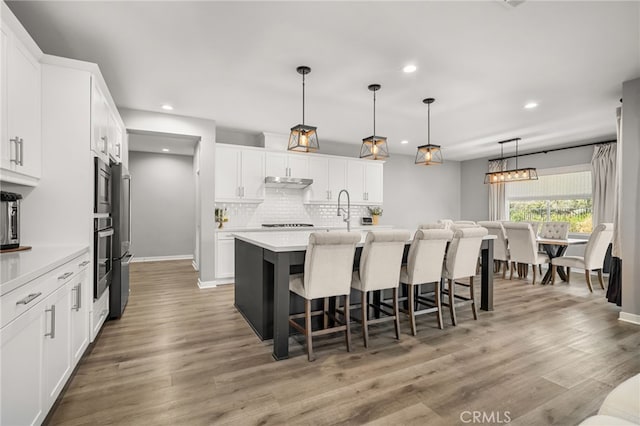 kitchen with a center island with sink, tasteful backsplash, a kitchen breakfast bar, pendant lighting, and white cabinets