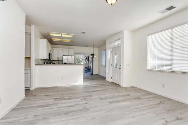 kitchen featuring appliances with stainless steel finishes, decorative backsplash, decorative light fixtures, white cabinets, and light hardwood / wood-style flooring