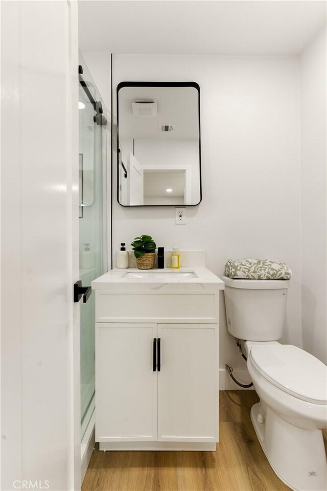 bathroom with toilet, vanity, wood-type flooring, and a shower with door