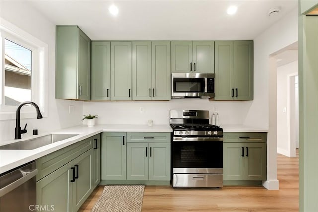 kitchen with green cabinets, appliances with stainless steel finishes, light hardwood / wood-style floors, and sink