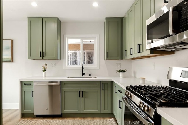 kitchen with light hardwood / wood-style flooring, appliances with stainless steel finishes, sink, and green cabinets