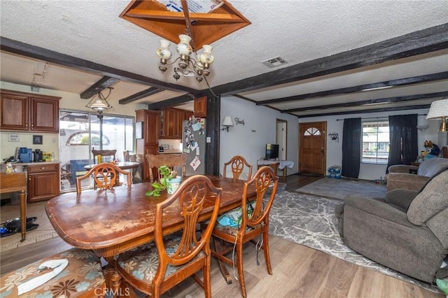 dining space featuring light hardwood / wood-style floors, a textured ceiling, beam ceiling, and an inviting chandelier