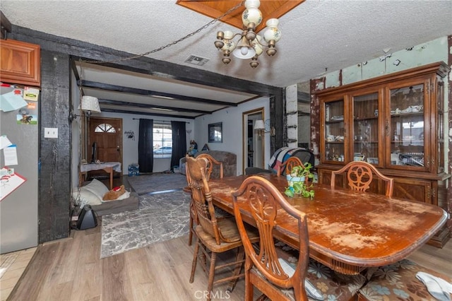 dining space with beam ceiling, a notable chandelier, a textured ceiling, and light hardwood / wood-style floors