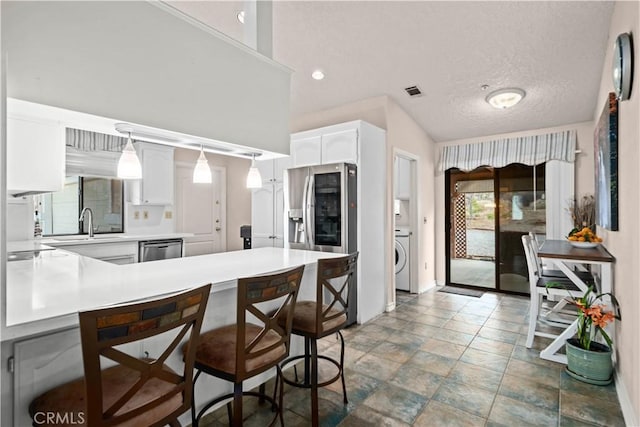 kitchen featuring washer / dryer, stainless steel appliances, a kitchen bar, and white cabinets