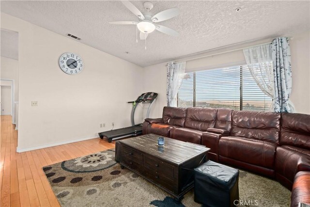 living room featuring ceiling fan, light wood-type flooring, and a textured ceiling