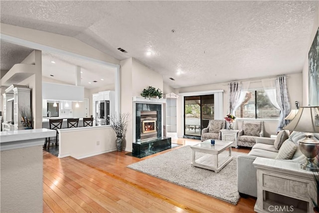 living room featuring vaulted ceiling, a high end fireplace, a textured ceiling, and wood-type flooring