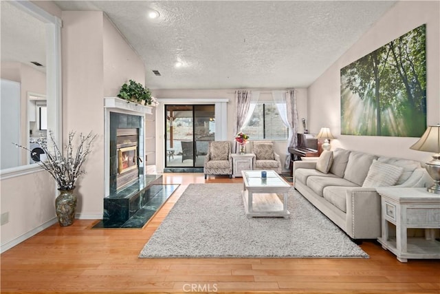 living room featuring vaulted ceiling, a fireplace, a textured ceiling, and hardwood / wood-style floors