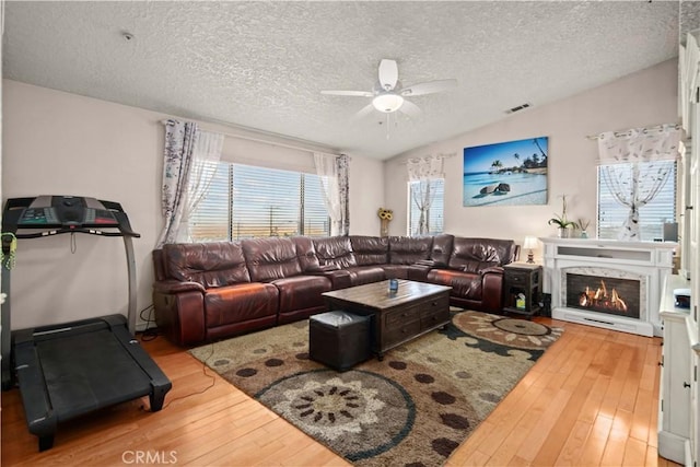 living room with hardwood / wood-style floors, lofted ceiling, a premium fireplace, and a textured ceiling