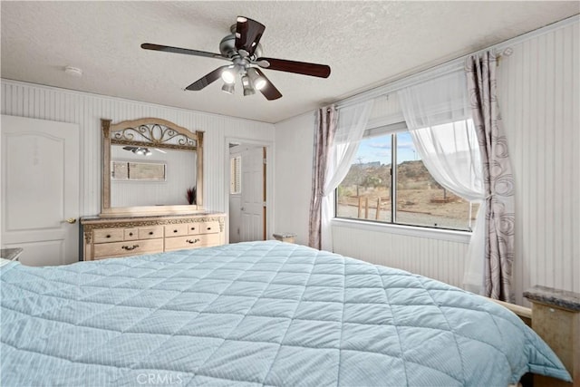 bedroom featuring ceiling fan, a textured ceiling, and wooden walls