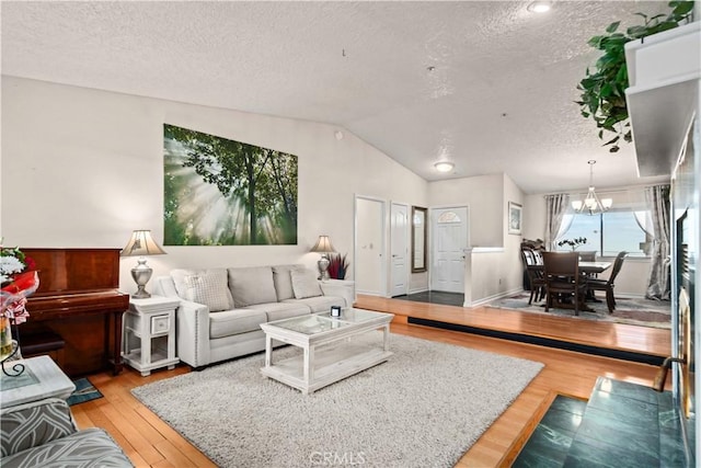 living room with light hardwood / wood-style floors, a textured ceiling, lofted ceiling, and a notable chandelier