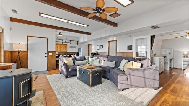 living room with hardwood / wood-style floors, a wood stove, wood walls, ceiling fan, and beam ceiling