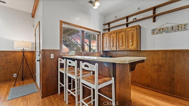 bar featuring vaulted ceiling, wooden walls, and light hardwood / wood-style flooring