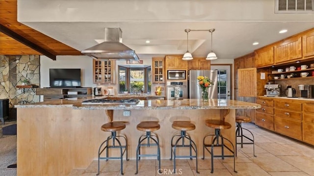 kitchen with island exhaust hood, appliances with stainless steel finishes, light stone counters, and a kitchen breakfast bar