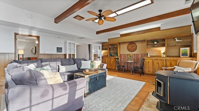 living room with wood walls, a wood stove, light wood-type flooring, beam ceiling, and built in shelves