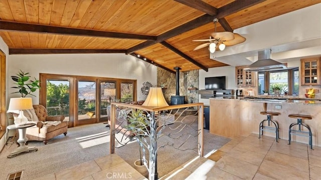 interior space featuring kitchen peninsula, island exhaust hood, wooden ceiling, a wood stove, and vaulted ceiling with beams