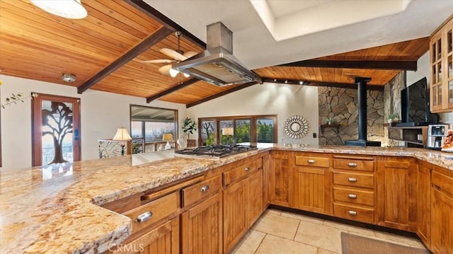 kitchen with vaulted ceiling with beams, stainless steel gas stovetop, a wood stove, and wooden ceiling