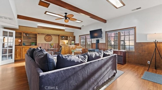 living room with ceiling fan, light hardwood / wood-style floors, beamed ceiling, and wooden walls