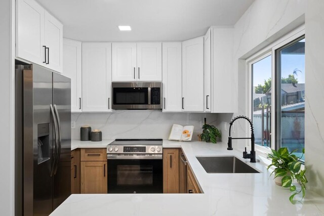 kitchen with white cabinetry, stainless steel appliances, tasteful backsplash, light stone countertops, and sink