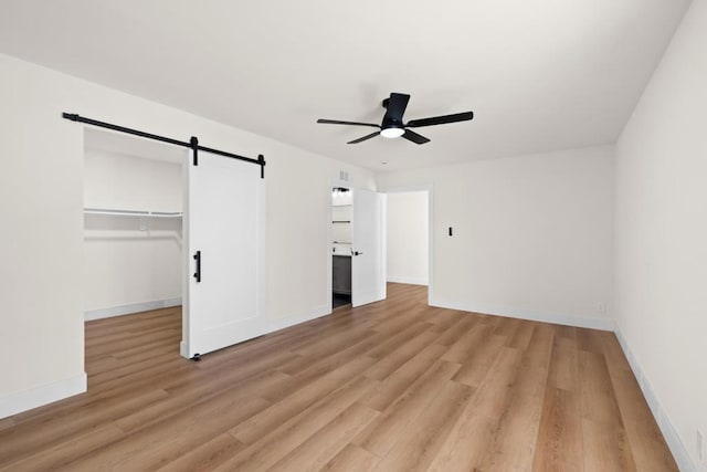 unfurnished bedroom with light hardwood / wood-style floors, a closet, a barn door, a walk in closet, and ceiling fan