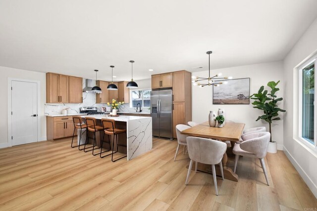 kitchen with appliances with stainless steel finishes, hanging light fixtures, a kitchen island, wall chimney exhaust hood, and sink