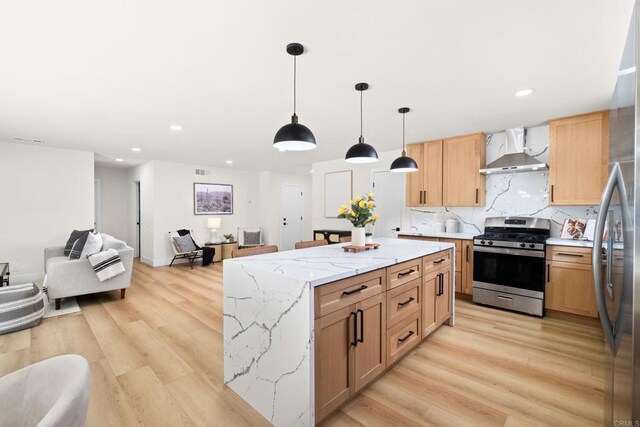 kitchen featuring stainless steel appliances, decorative backsplash, light hardwood / wood-style flooring, wall chimney range hood, and decorative light fixtures