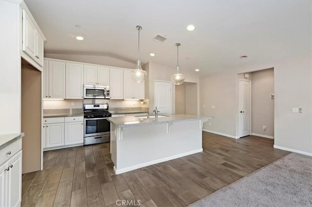 kitchen featuring stainless steel appliances, a sink, white cabinets, hanging light fixtures, and a center island with sink