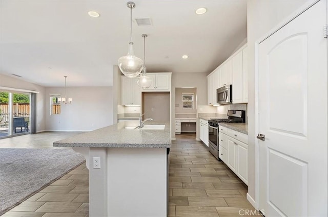 kitchen with open floor plan, stainless steel appliances, a kitchen island with sink, and white cabinets