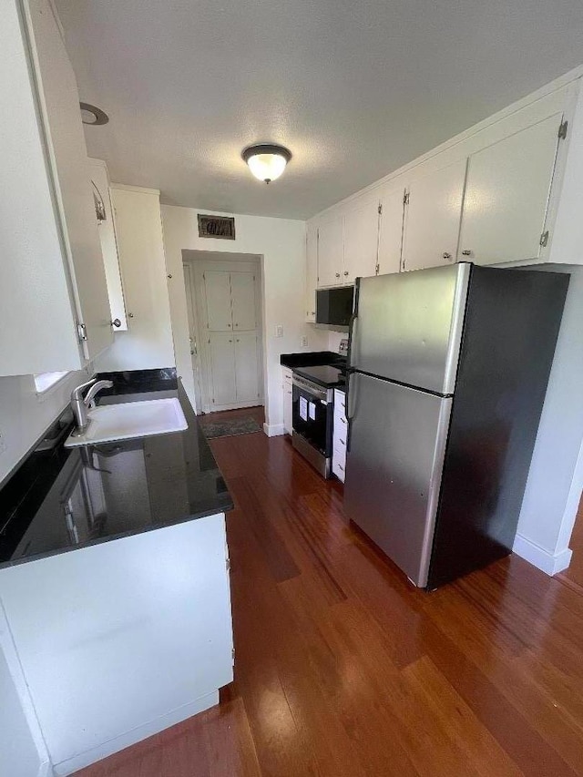 kitchen with dark wood-type flooring, white cabinetry, stainless steel appliances, and a textured ceiling