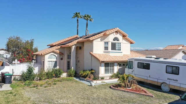 mediterranean / spanish home with a front lawn, stucco siding, a tile roof, and fence