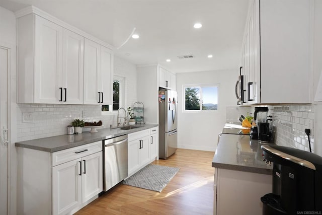 kitchen with backsplash, sink, white cabinetry, light wood-type flooring, and stainless steel appliances