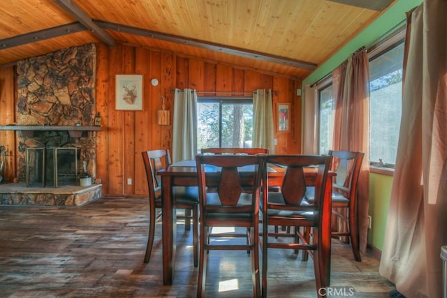 dining room with a healthy amount of sunlight, a fireplace, wood walls, and lofted ceiling with beams