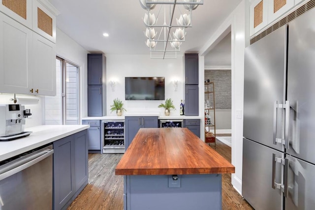 kitchen with appliances with stainless steel finishes, a kitchen island, decorative light fixtures, wood counters, and wine cooler