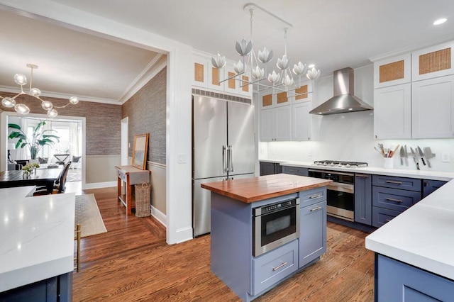 kitchen featuring pendant lighting, white cabinets, a center island, wall chimney range hood, and stainless steel appliances