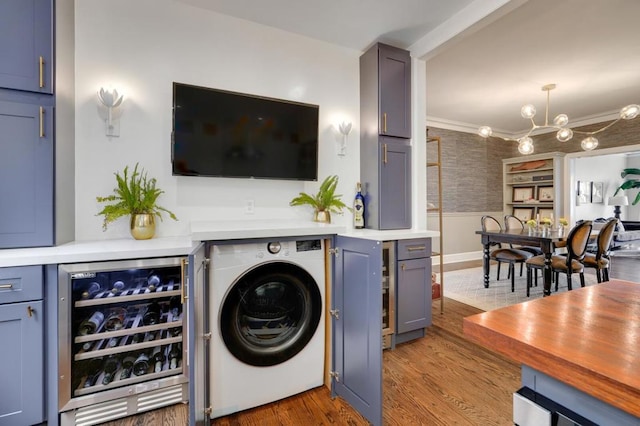 clothes washing area with washer / clothes dryer, beverage cooler, ornamental molding, light hardwood / wood-style floors, and an inviting chandelier