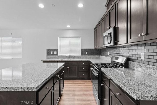 kitchen with appliances with stainless steel finishes, sink, light stone counters, and light hardwood / wood-style floors