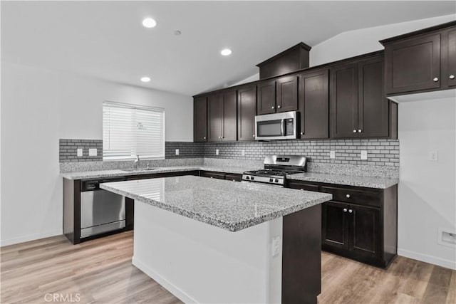 kitchen with lofted ceiling, a center island, sink, light stone countertops, and appliances with stainless steel finishes