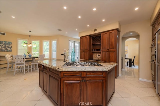 kitchen featuring light stone countertops, pendant lighting, a center island, a notable chandelier, and stainless steel gas stovetop