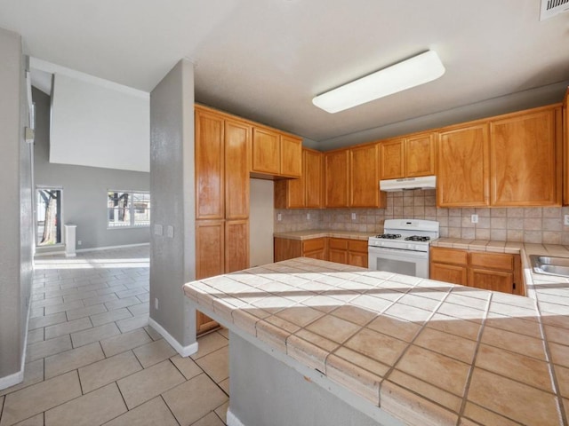 kitchen with kitchen peninsula, white range with gas cooktop, tile counters, and light tile patterned flooring