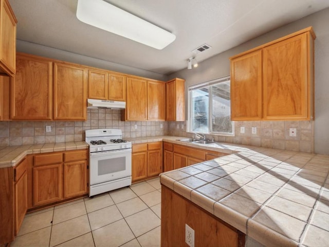 kitchen featuring tasteful backsplash, sink, white gas stove, tile counters, and light tile patterned floors