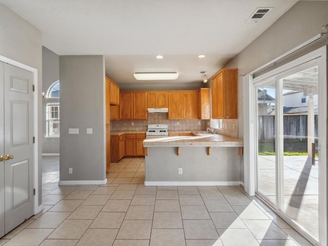 kitchen featuring white stove, tile countertops, kitchen peninsula, tasteful backsplash, and light tile patterned flooring