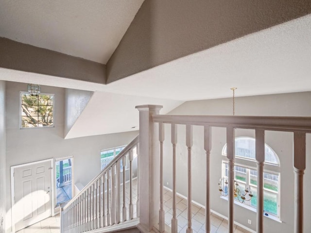 stairs with lofted ceiling, an inviting chandelier, and a textured ceiling