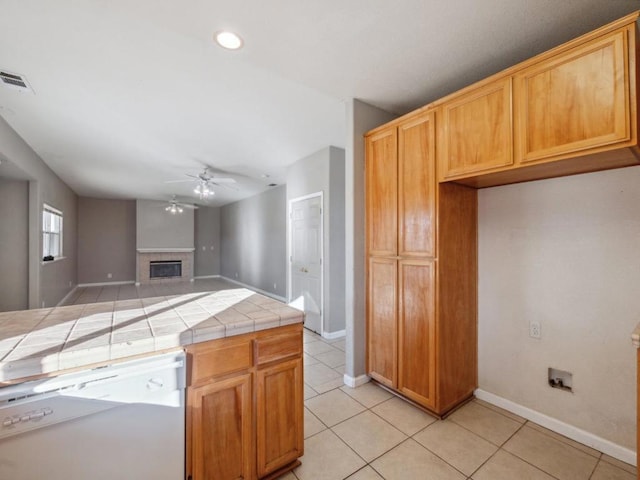 kitchen featuring dishwasher, a fireplace, tile countertops, ceiling fan, and light tile patterned floors